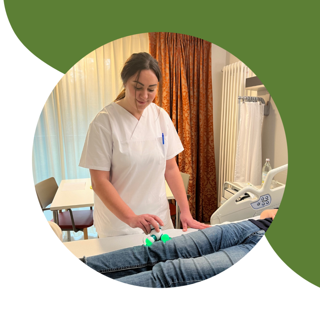 Foto einer Pflegefachkraft am Patientenbett mit einem kleinen Massagegerät, welches sie auf das Bein einer Patientin hält. Das Foto befindet sich in einem kreisrunden Rahmen und die obere rechts Hälfte des Bildes ist mit einem grünen Designelement hinterlegt.