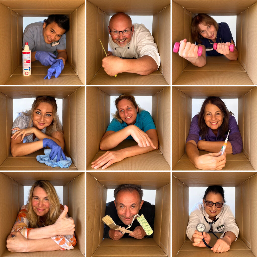 Foto der "Klinik-Familie" Zusammenschnitt aus 9 einzelnen Fotos in je einem Karton. Neun Mitarbeitende verschiedenen Berufsgruppen repräsentieren die Vielfalt in der Klinik Wartenberg. Oben links ist eine Pflegefachkraft mit Handschuhen und Desinfektionsspray zu sehen, oben in der Mitte ein Koch mit einem Messer, oben rechts eine Physiotherapeutin mit Hanteln, mittig links eine Reinigungskraft mit einem Putzlappen, in der Mitte eine Patientenbetreuerin, rechts in der Mitte eine medizinische Fachangestellte mit einer Spritze, unten links eine Mitarbeiterin der Sozialen Beratung, unten in der Mitte ein Haustechniker mit Pinsel und Rolle und unten rechts eine Ärztin mit einem Stethoskop. Die neun einzelnen Fotos wurden zu einem Raster zusammengesetzt, sodass es so aussieht aus würden die Mitarbeitenden in einem Block aus 9 Kartons sitzen.