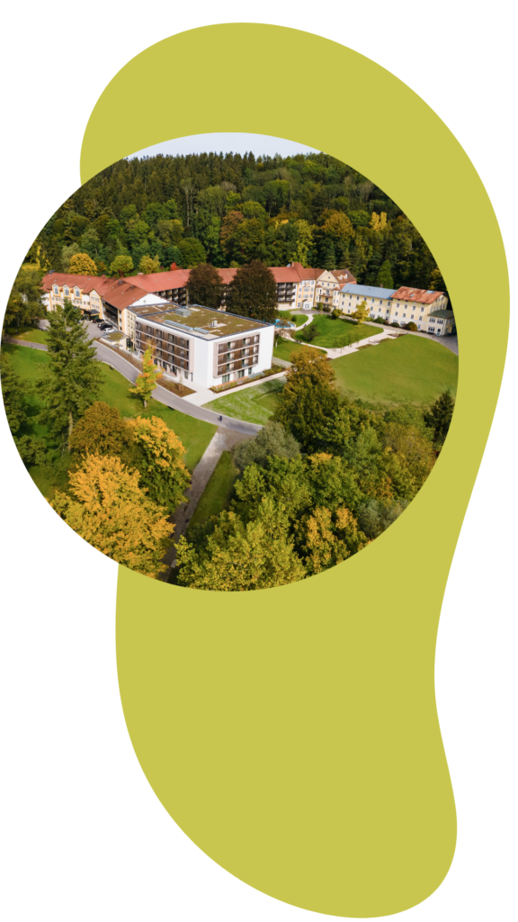 Luftbild der Klinik Wartenberg in einem kreisrunden Rahmen. Im Hintergrund ein helsgrünes, längliches Designelement.
